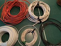 Five coiled lengths of cable in white, red, and black sheathing on a green table surface