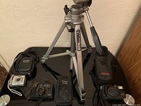 Photo showing the four items: Canon Powershot digital camera, Canon AF35M film camera, Pentax Zoom 105R film camera, and Velbon tripod together on a black surface.