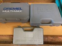 Three closed hard plastic cases: Dremel Multi-Max case, Dremel Contour Sander case, and 25-piece rubber sanding drum set case.