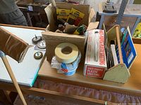 Top-down photo showing box of drywall tools, rolls of drywall tape, masking tape, plastic sheeting box, and wooden tool carrier.