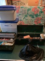 Overview of two Coleman coolers (white with blue lids), one rusty metal tackle box open with fishing gear, one plastic tackle box closed, and the black waterproof Sou'wester hat on table.