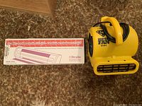 Photo showing the Simplex Dimplex electric baseboard heater box with product details and the yellow Soleaire Super Fan placed next to it.