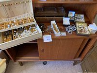 Overview of white faux-leather jewelry box, wooden tray and assorted costume jewelry on cabinet