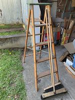 Wooden stepladder with paint splatters and two wooden push brooms leaning against it.