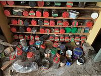 Wide view of wooden shelf with multiple cylindrical containers with red lids labeled for nails, hooks, bolts of various sizes and types