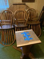 Dining table disassembled showing the pedestal base and removable round top with visible attachment hardware. Six oak dining chairs positioned behind the table parts.