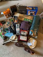 Overview of all items laid out on floor showing tent bag, air bed box, horseshoes box, binoculars, walkie talkies, hats, boots, flask, umbrellas, compass, telescope and electric throw.