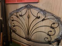 Full view of the brass decorative headboard wrapped in protective bubble wrap, leaning against a wood-paneled wall.