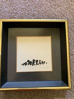 Framed artwork showing black silhouette abstract shapes with gold-trimmed frame.