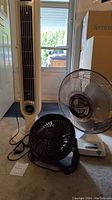 Photo showing all three fans together: tall white tower fan, medium white pedestal fan, and small black tabletop fan.