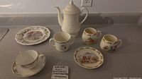 Wide view of all items including Bunnykins cups, plate, Staffordshire cup and saucer, Royal Doulton plate, and Wedgewood coffee pot.