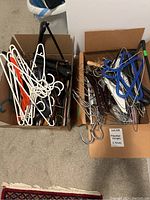 Two boxes filled with mixed clothes hangers including plastic in white, black, orange; metal wire hangers; and wooden hangers in dark and natural finishes.