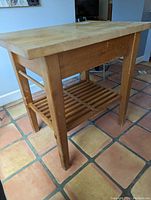 Butcher's block island angled view showing thick solid wood top, slatted shelf, and wood legs with wear.