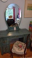 Front view of green dressing table with oval mirror and floral upholstered balloon back chair.