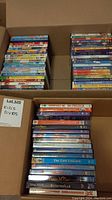 Three cardboard boxes filled with multiple stacks of kid-friendly DVDs, showing colorful spines with titles and Disney movies included.