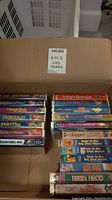 Photo of 17 kid-friendly VHS tapes arranged in a box, titles visible including classic Disney movies and children series
