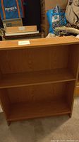 Front view of small light brown wooden bookshelf showing two shelves and wood grain finish.