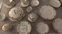 Overview of nearly complete 4 person Limoges dinnerware set including plates, cups, saucers, covered tureen and bowls with floral and gold designs.