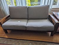 Front view of grey loveseat with wooden armrests and two seat cushions.