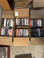Three open cardboard boxes filled with DVD and Blu-ray cases arranged in rows