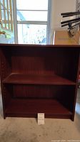 Front view of the small dark brown bookshelf showing two shelves and inner side panels with adjustable shelf holes.
