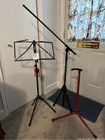 Photo showing all three stands: sheet music stand, microphone stand with boom arm, and red and black guitar stand.