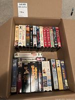 One open box containing 22 VHS movies arranged in two rows displaying their spines and front cover art for identification.
