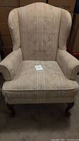 Full front view of cream patterned wingback chair showing fabric condition and overall shape.