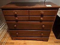 Front view of the brown wood dresser showing six drawers with round knobs and visible scratch marks on the surface.