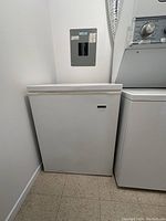 Front view of white chest style deep freezer standing on the floor next to dryer.