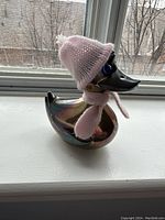 Sterling silver duck figurine with metallic finish and pink knitted hat and scarf.