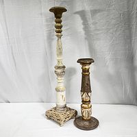 Two hand carved wooden candle holders photographed front side by side on white fabric background showing distressed paint and carved details