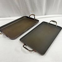 Two large rectangular cast iron pans with dual handles shown on white fabric background.
