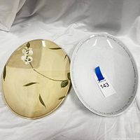 Two large oval platters seen side by side on white fabric background, front and back visible.