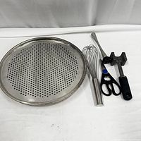 Overhead view of removable perforated pizza tray alongside whisk, kitchen scissors and meat tenderizer mallet