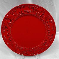 Top view of large round red platter showing raised baroque scroll design along the rim.