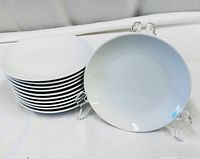 Set of 11 small white plates stacked and one plate on display stand showing size and shape.
