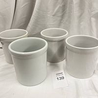 Four white stoneware utensil caddies arranged in a row, showing their exterior cylindrical shape and slightly flared rims.