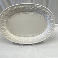 Full view of off white oval serving platter with embossed fruit and vine pattern around the edge.