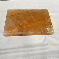 Rectangular pink Himalayan salt block with visible veining and a crack on one corner, laying flat on white fabric background.