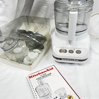 KitchenAid food processor unit, accessories in plastic container, and user manual in front