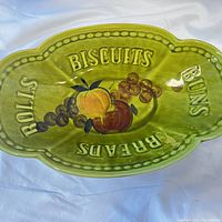 Top view of green ceramic bread bowl with embossed words BISCUITS, BUNS, BREADS, ROLLS and painted fruit in center.