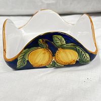 Close-up side view showing hand-painted yellow lemons with green leaves on a deep blue background and white scalloped edges with gold trim.