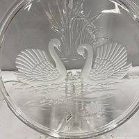 Close-up image showing detailed raised glass design of two swans and lotus flowers on the clear glass cake plate.