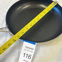 Top view of the pan showing the black nonstick inner surface and the measuring tape across it indicating about 11 inches diameter.