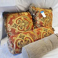 Two square paisley woven chenille throw pillow covers in brick red with fringe, matching bolster pillow, and rolled fabric piece arranged on white background