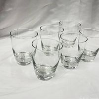 Six clear vintage rocks glasses with controlled bubble bases arranged on white cloth background.