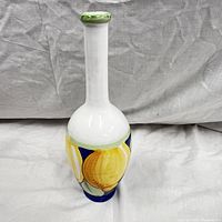 Front view of the vintage Italian ceramic vase showing hand painted yellow fruit on blue background with long white neck and green rim.