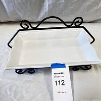 White ceramic serving tray with scalloped edges held in a black iron rack with scrollwork details, shown from a front angle with MaxSold tag visible.