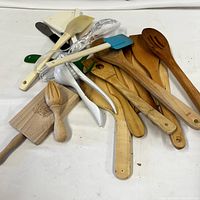 Top view of assorted wooden kitchen utensils including spoons, spatulas, citrus reamers, and some plastic kitchen tools arranged on a white cloth.
